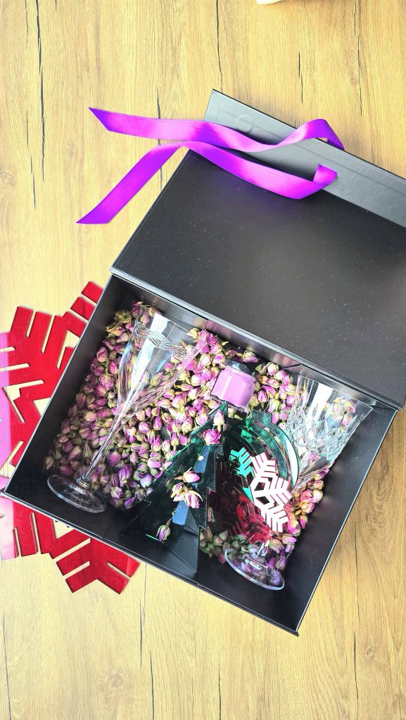 Premium luksuzna kutija sa sušenom Damask ružom (božur), Kutija s ljubičastom ukrasnom vrpcom ( zatvaranje na magnet) sadrži 2 kristalne čaše na stalku, 2 unikatna podloška za čaše, ručno izrađena svijeća s mirisom esencijalnih ulja po izboru te unikatni božićni ukras koji će krasiti dom ili poslovni prostor.